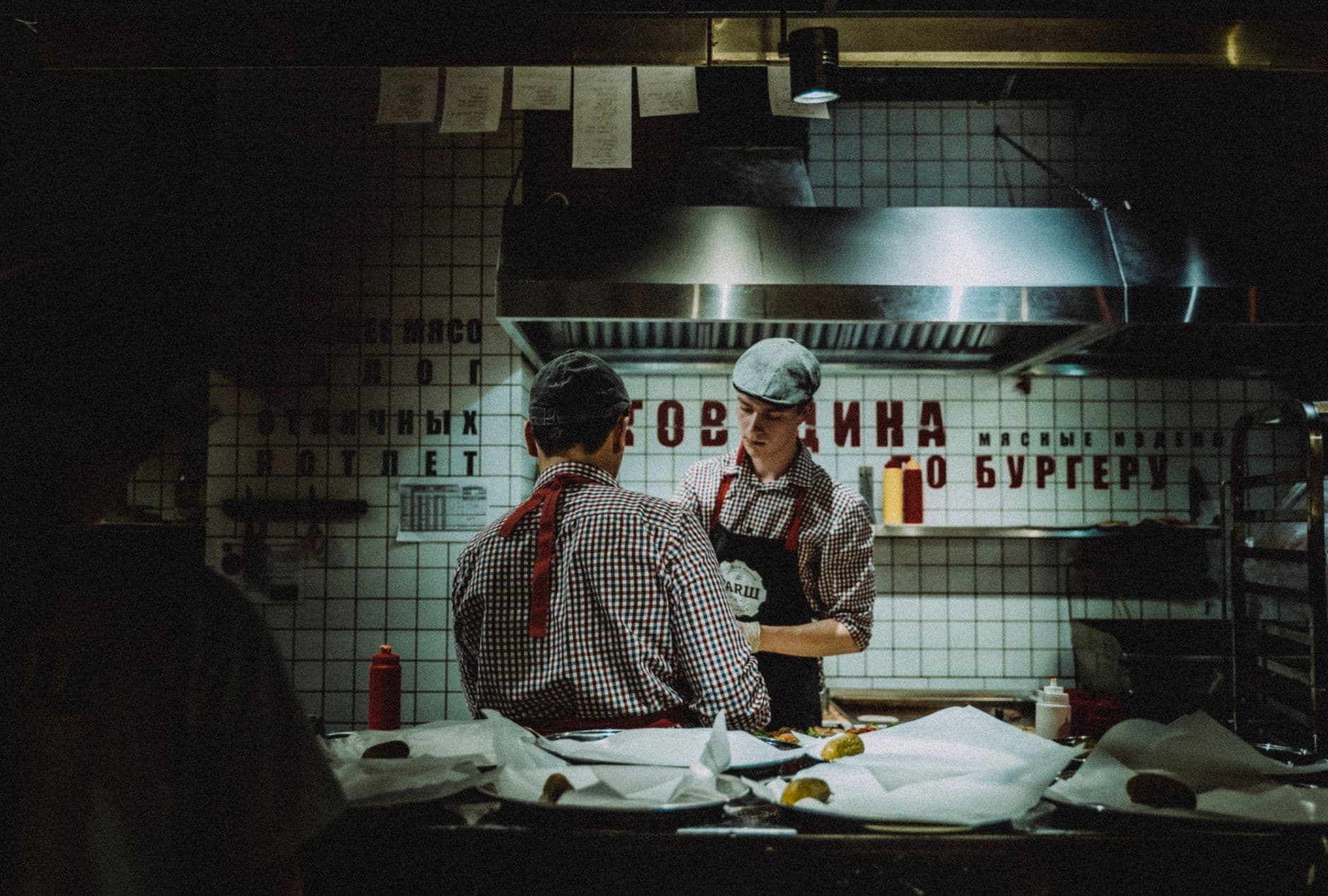 A professional technician checks a rodent monitoring station on a restaurant kitchen floor.